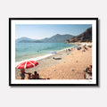 Fine art photography titled 'Magnums' by Venturer Studios, featuring a sunlit beach in Western Turkey dotted with vibrant, colorful umbrellas. The bright coastal scene is captured in a deep black gallery frame.