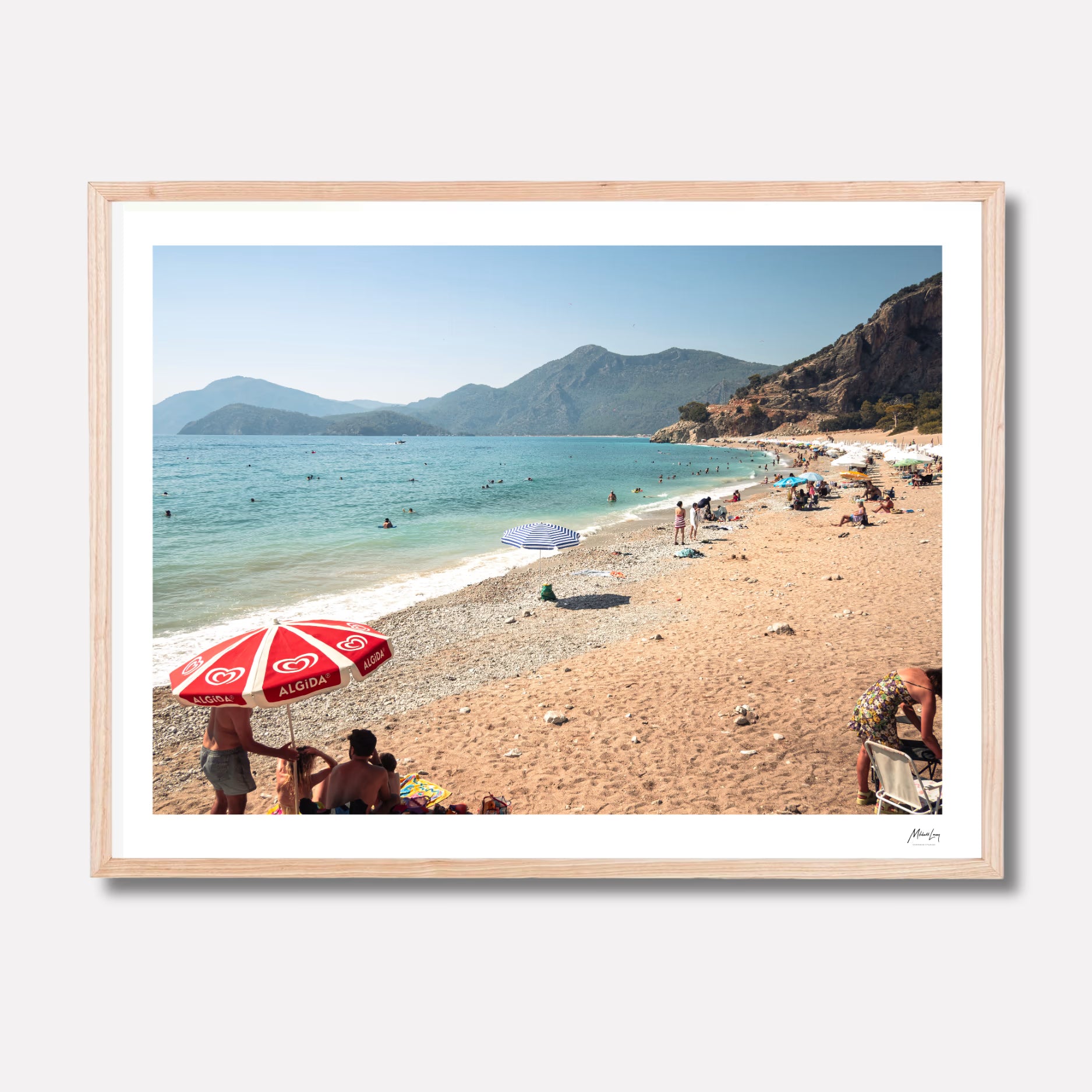 Framed photograph of a beach scene with people, umbrellas, and mountains.