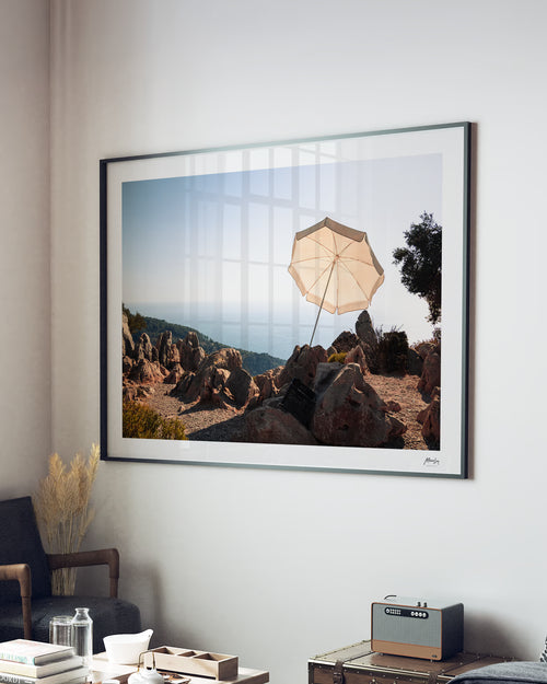 Framed artwork of a landscape with an umbrella on a rocky hillside, displayed in a living room.