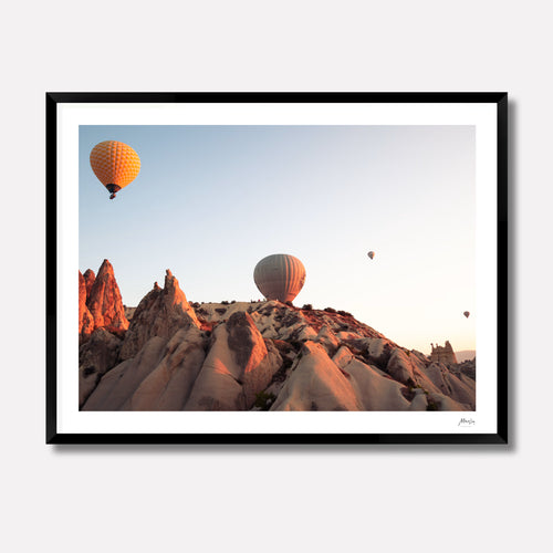 Fine art photography titled 'Fairy Meadows' by Venturer Studios, capturing hot air balloons drifting over a misty, cold valley floor at sunrise in Cappadocia. The atmospheric landscape is showcased in a premium black gallery frame.
