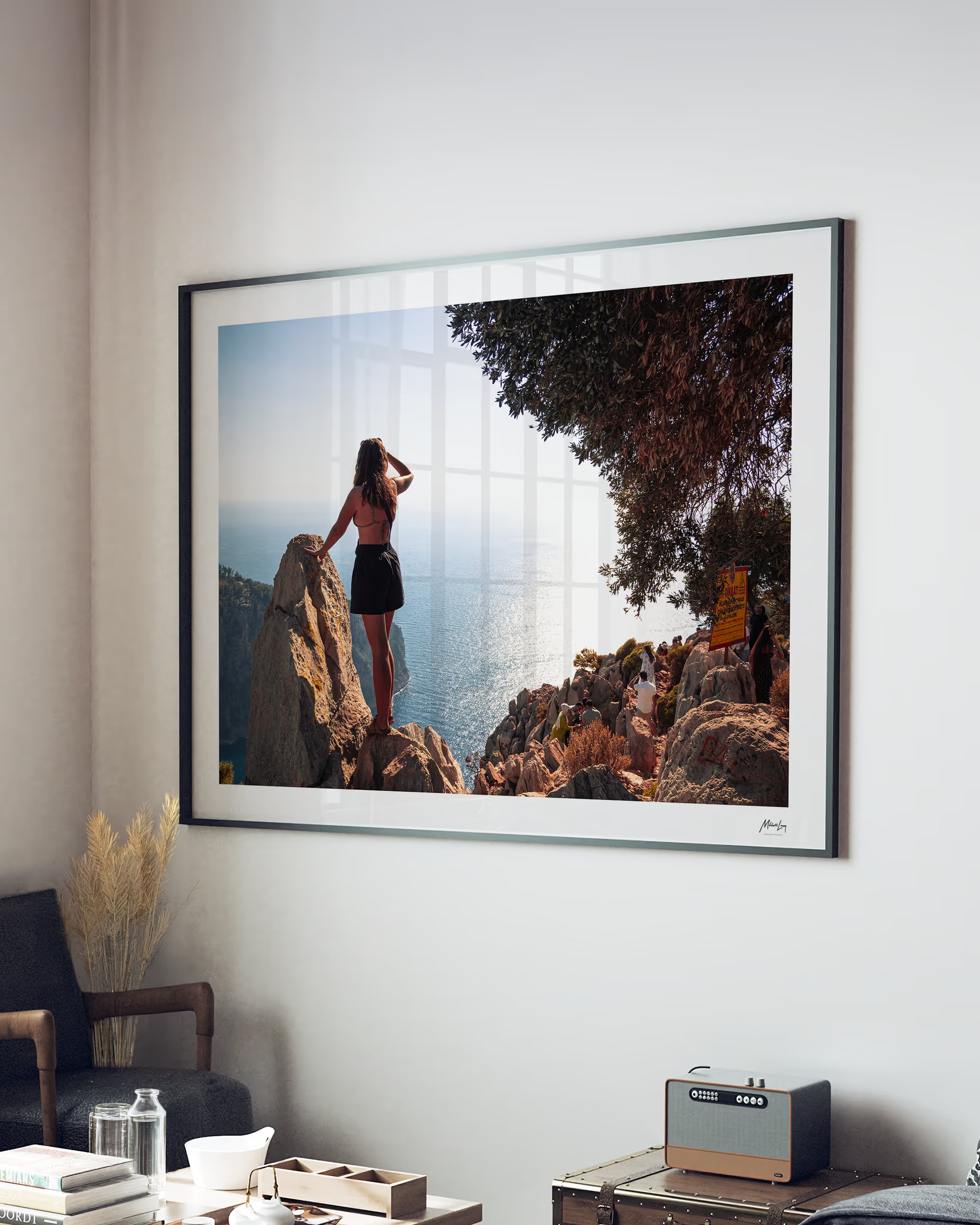 Framed artwork of a woman on rocks hanging on a wall in a room.