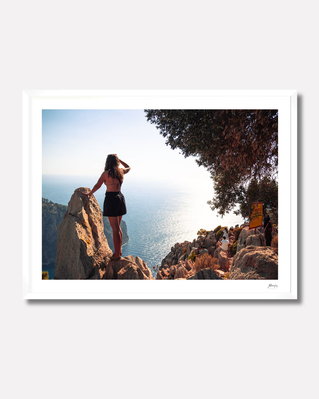Person standing on a rock overlooking the ocean with a framed picture of a scenic view.