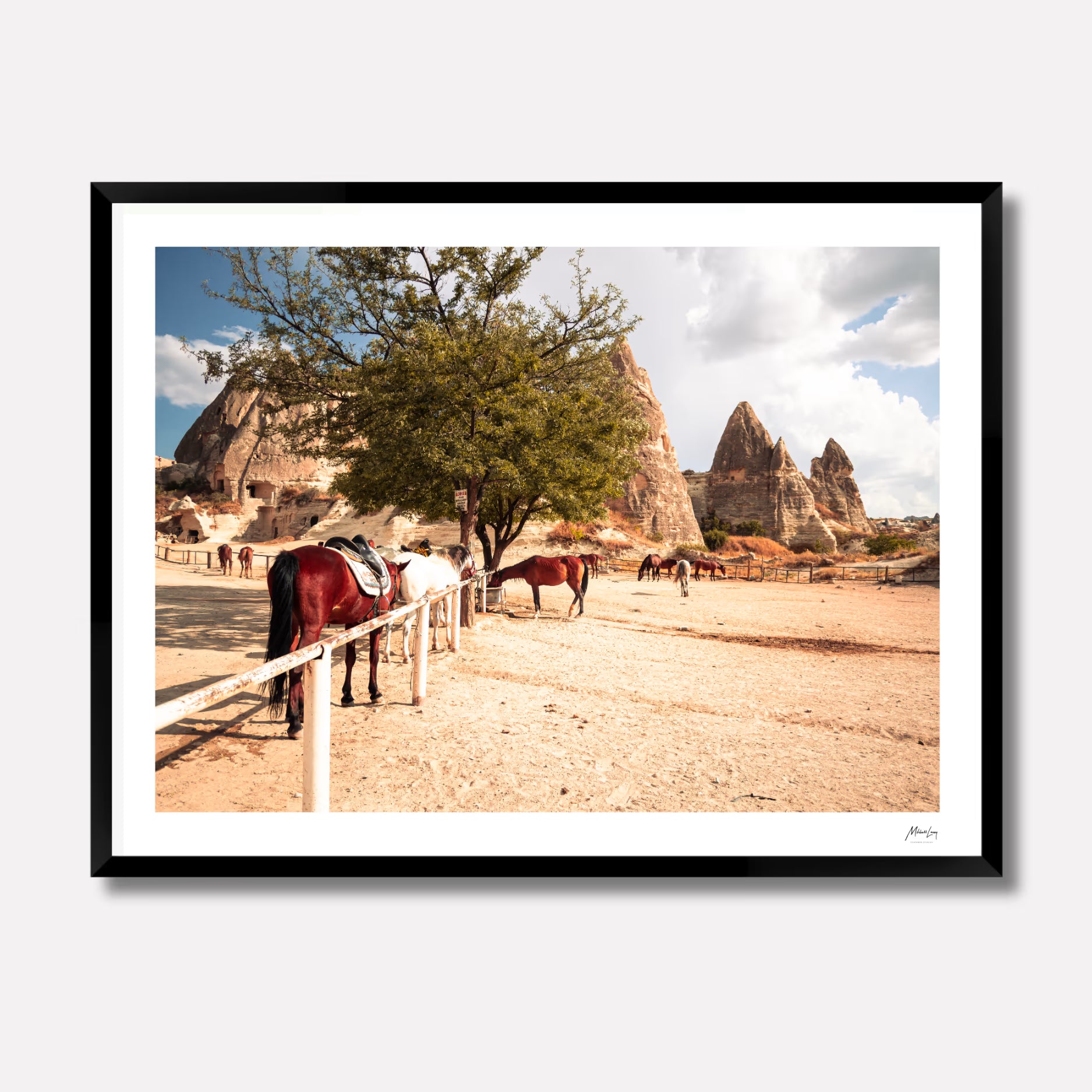 Fine art print of wild horses running through the dusty desert landscape of Cappadocia, Turkey, under a soft sky. Captured by Venturer Studios and presented in a sleek black gallery frame.
